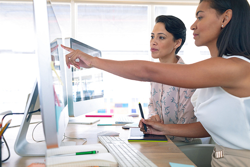 Side view of diverse female graphic designers discussing on computer at desk in a modern office