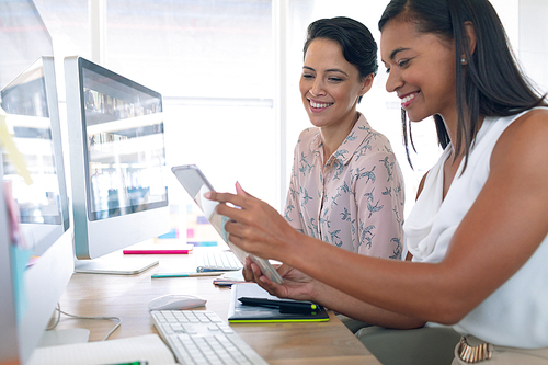 Side view of diverse female graphic designers discussing on digital tablet at desk in a modern office