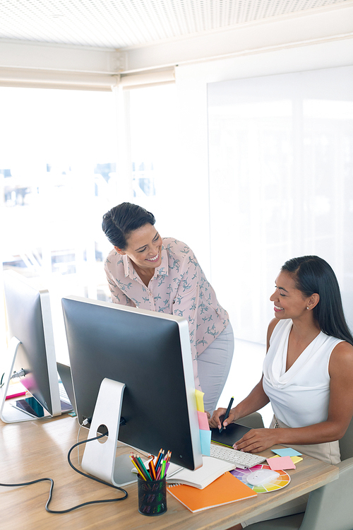 Side view of happy diverse female graphic designers talking with each other at desk in a modern office