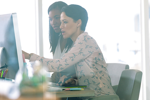 Side view of diverse female graphic designers discussing on computer at desk in a modern office