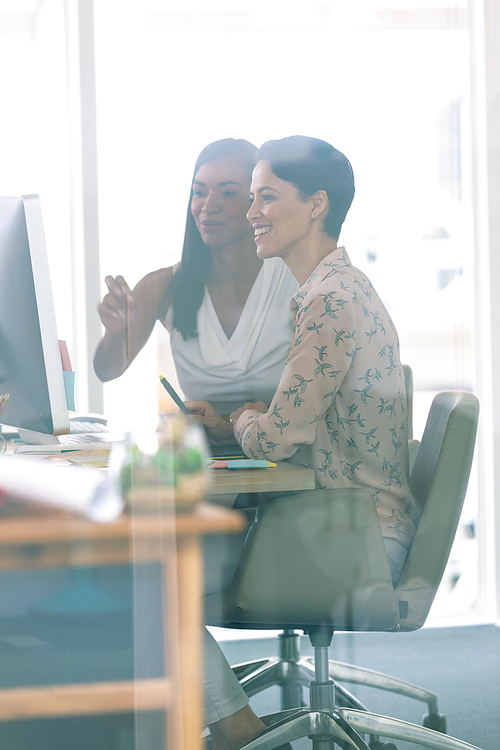 Side view of diverse female graphic designers discussing on computer at desk in a modern office