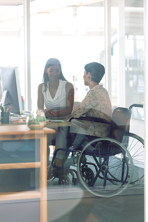 Side view of diverse female graphic designers interacting with each other at desk in a modern office