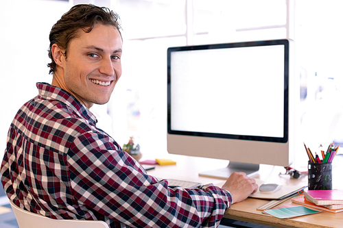 Side view of happy Caucasian male graphic designer  while working on computer at desk in a modern office