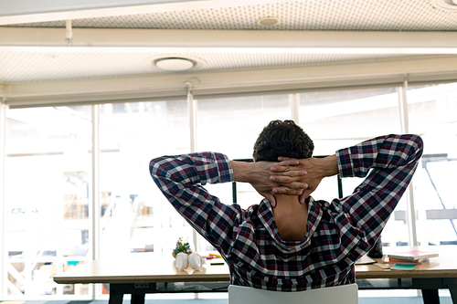 Rear view of Caucasian male graphic designer with hands behind head sitting on chair in a modern office