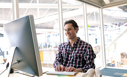 Side view of happy Caucasian male graphic designer working on computer at desk in a modern office