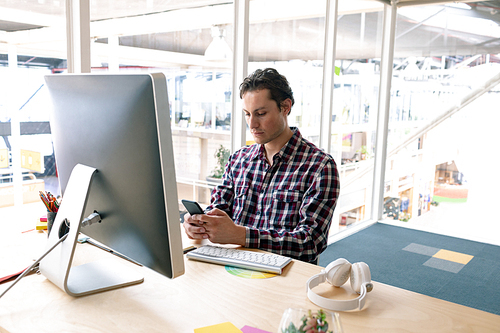 Front view of Caucasian male graphic designer using mobile phone at desk in a modern office