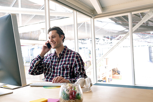 Side view of happy Caucasian male graphic designer talking on mobile phone at desk in a modern office