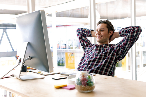 Side view of happy Caucasian male graphic designer with hands behind head sitting on chair in a modern office