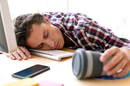 Front view of tired Caucasian male graphic designer sleeping on desk in a modern office