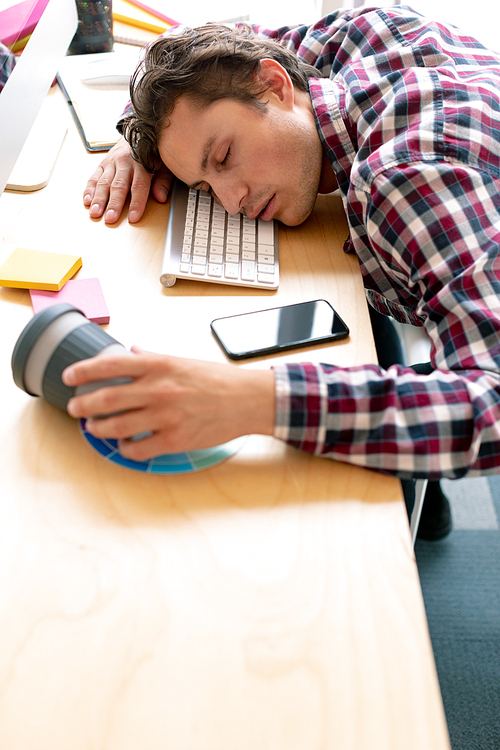 High view of tired Caucasian male graphic designer sleeping on desk in a modern office