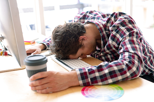 Side view of tired Caucasian male graphic designer sleeping on desk in a modern office