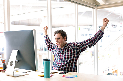 Side view of happy Caucasian male graphic designer celebrating success at desk in a modern office