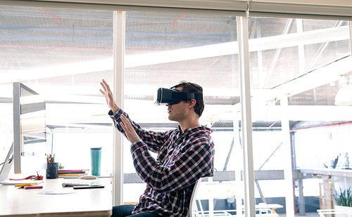 Side view of Caucasian male graphic designer using virtual reality headset at desk in office