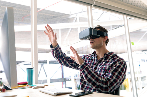 Side view of Caucasian male graphic designer using virtual reality headset at desk in office