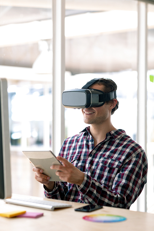 Side view of Caucasian male graphic designer using virtual reality headset while working on digital tablet at desk in office