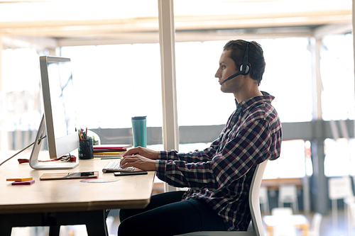 Side view of Caucasian male graphic designer working on computer at desk in office