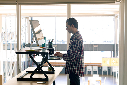 Side view of Caucasian male graphic designer working on computer at desk in office