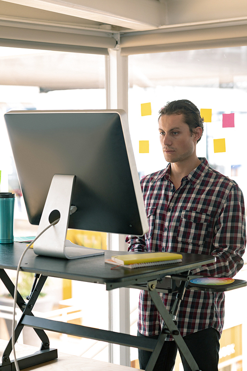 Side view of Caucasian male graphic designer working on computer at desk in office