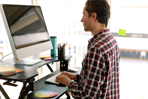 Side view of Caucasian male graphic designer working on computer at desk in office