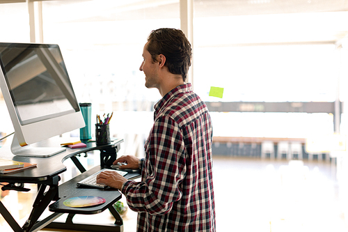 Side view of Caucasian male graphic designer working on computer at desk in office