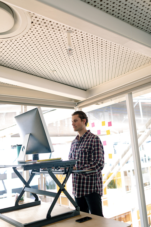 Side view of Caucasian male graphic designer working on computer at desk in office