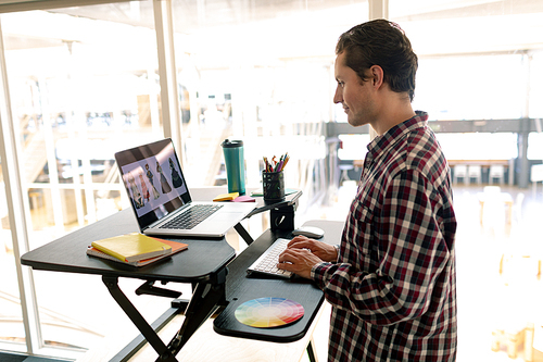 Side view of Caucasian male graphic designer working on laptop at desk in office