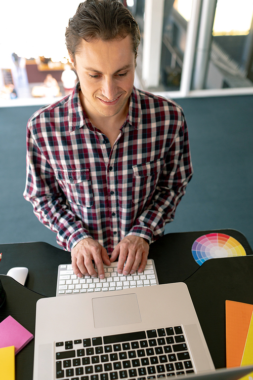 High view of Caucasian male graphic designer working on laptop at desk in office