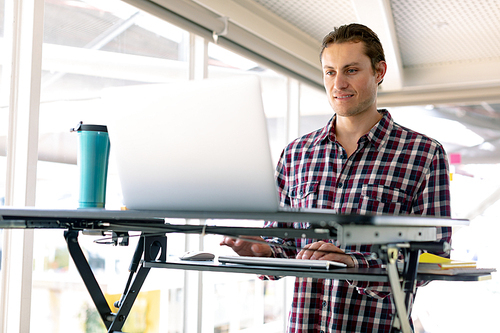 Front view of Caucasian male graphic designer working on laptop at desk in office