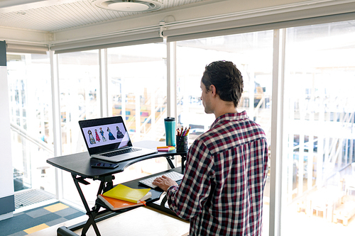 Rear view of Caucasian male graphic designer working on laptop at desk in office