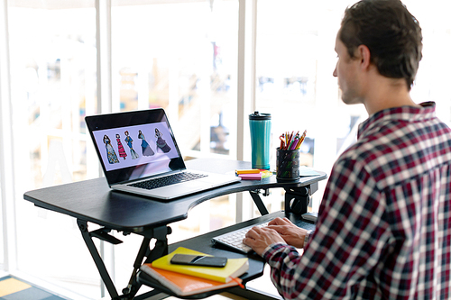 Side view of Caucasian male graphic designer working on laptop at desk in office