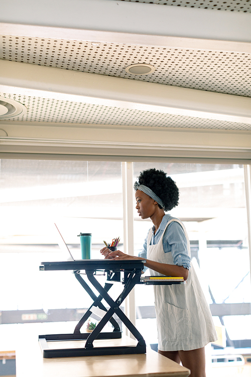 Side view of African american female graphic designer working on laptop at desk in office