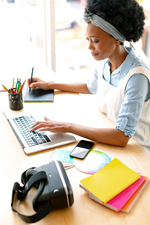 High view of African american female graphic designer using graphic tablet and laptop at desk in office