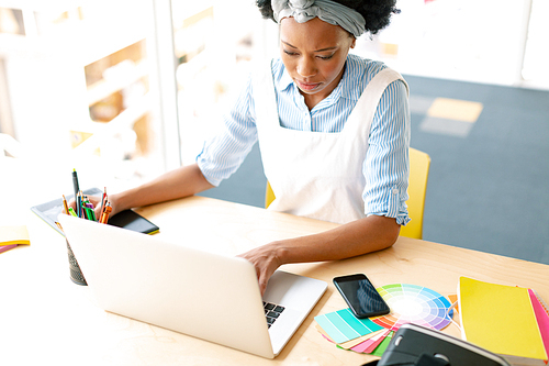 High angle view of African american female graphic designer using graphic tablet and laptop at desk in office