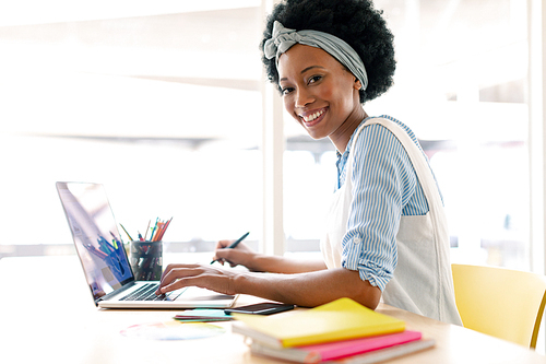 Side view of African american female graphic designer using graphic tablet and laptop at desk in office