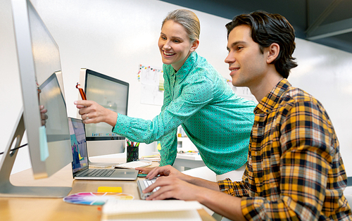 side view of Caucasian male and female graphic designer discussing over computer at desk in office