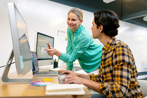 Side view of Caucasian male and female graphic designer discussing over computer at desk in office