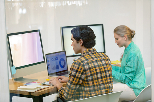 Rear view of Caucasian male and female graphic designer working on computer at desk in office