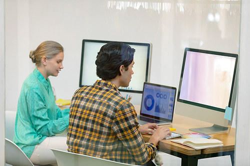 Rear view of Caucasian male and female graphic designer working on computer at desk in office