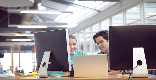 Front view of Caucasian male and female graphic designer discussing over computer at desk in office