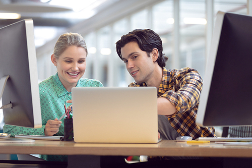 Front view of Caucasian male and female graphic designer discussing over computer at desk in office