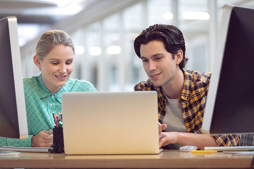 Front view of Caucasian male and female graphic designer discussing over computer at desk in office