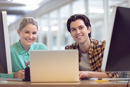 Front view of Caucasian male and female graphic designer discussing over computer at desk in office