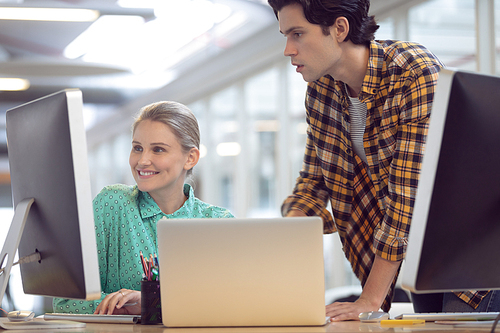 Side view of Caucasian male and female graphic designer discussing over computer at desk in office