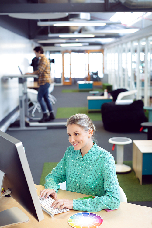 Side view of Caucasian female graphic designer working on computer at desk in office