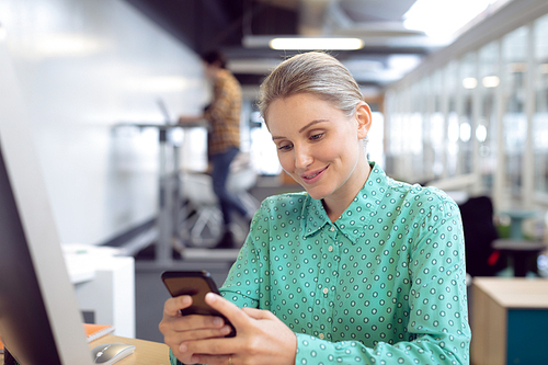 Front view of Caucasian female graphic designer using mobile phone at desk in office