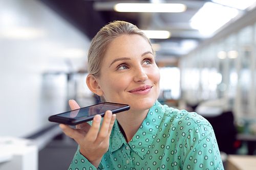 Front view of happy Caucasian female graphic designer talking on mobile phone in office