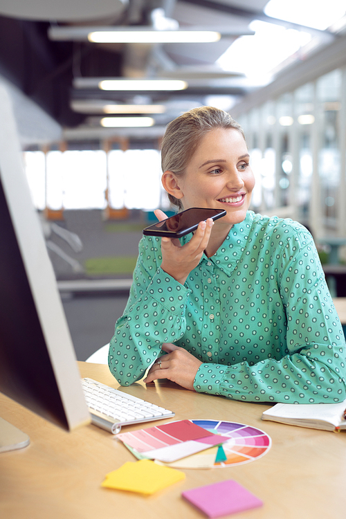 Front view of Caucasian female graphic designer talking on mobile phone at desk in office