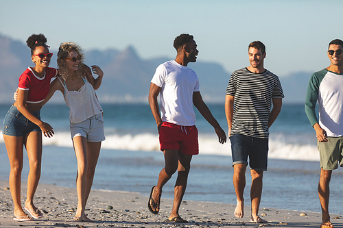 Front view of group of diverse happy friends walking together and having fun on the beach