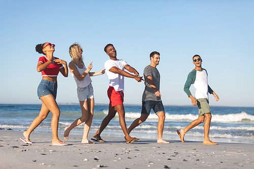 Side view of group of happy diverse friends walking together on the beach