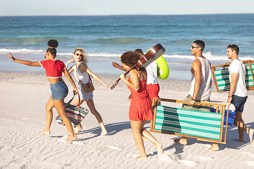 Side view of group of happy diverse friends walking together on the beach